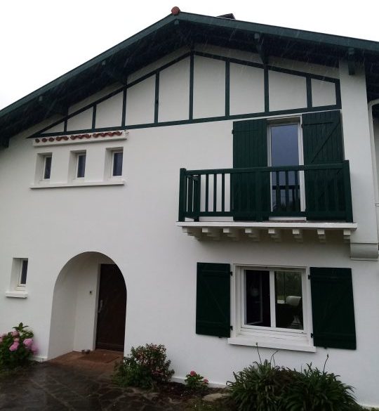 Maison blanche avec volets verts et balcon